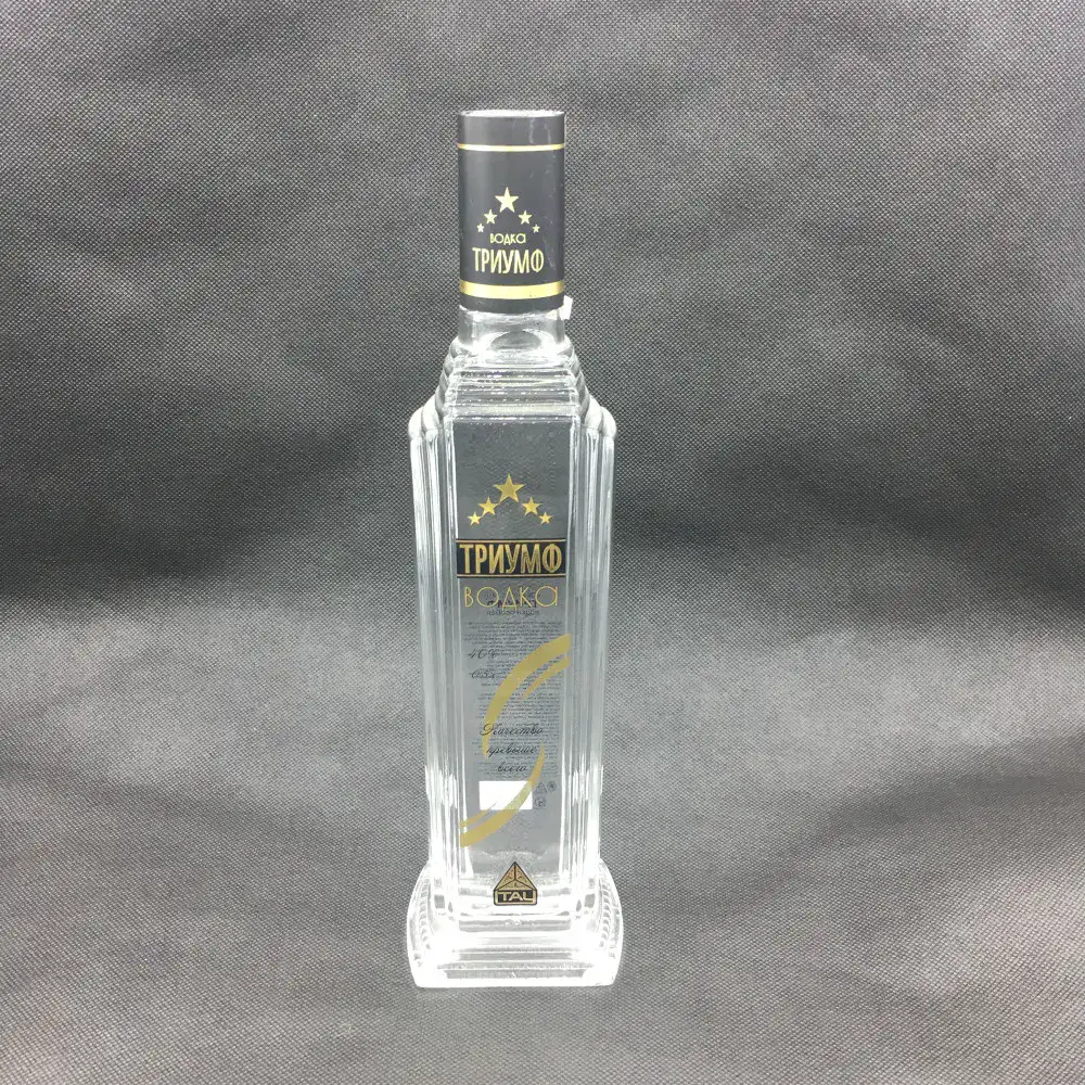 A 500ml square glass vodka bottle made of crystal-clear super flint glass, featuring a distinctive stepped shoulder, elegant vertical fluted ridges on the sides, a thick heavy base, and premium gold and black silk screen branding.