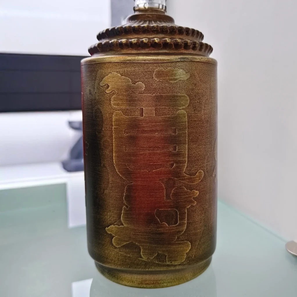 A custom spirits glass bottle showcasing a luxury antique bronze metallic color coating with a distressed brushed texture over an embossed Chinese character design.