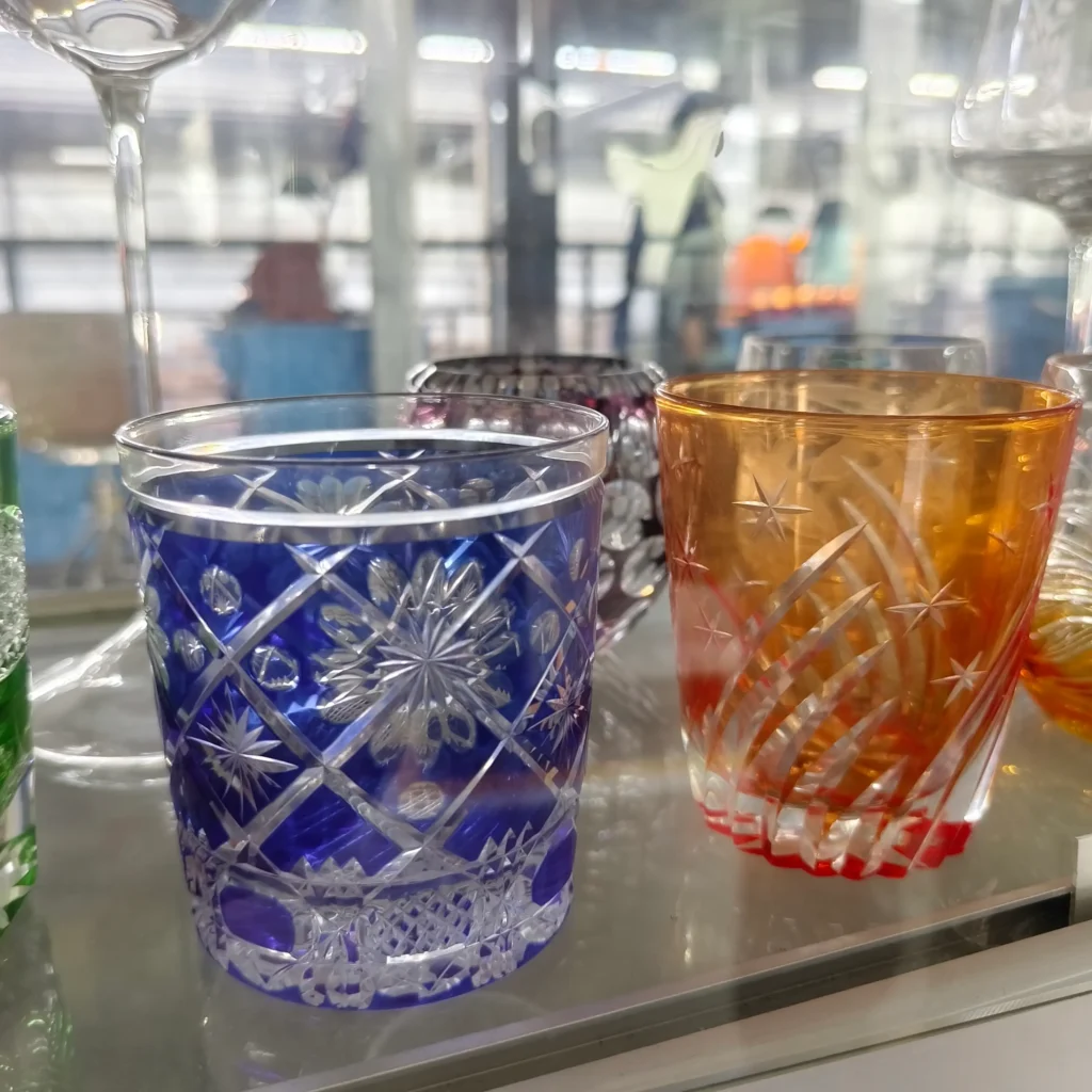 Premium hand-engraved crystal tumblers showcasing bespoke glass artistry, with one cobalt blue glass featuring precise geometric diamond-cuts and another amber glass featuring delicate engraved stars.