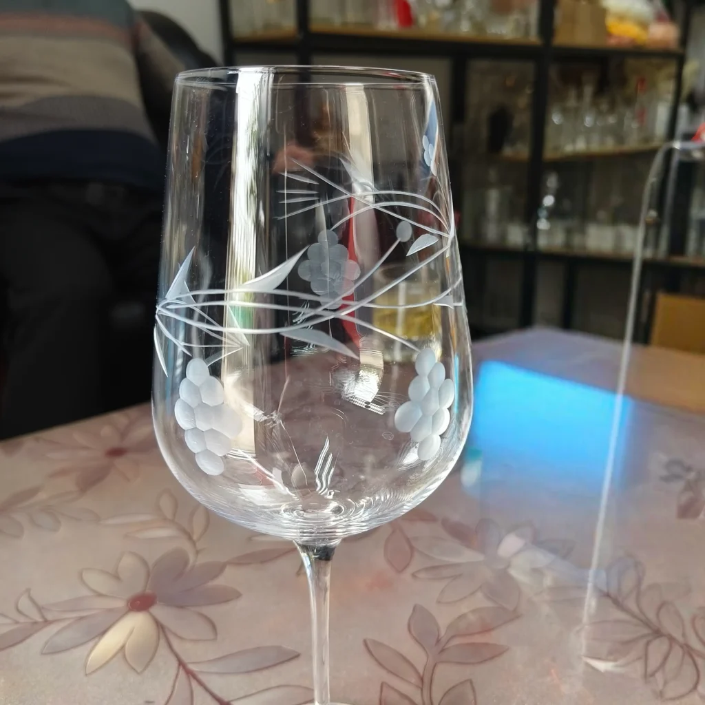 A clear stemware wine glass featuring detailed hand-engraved floral and grape vine patterns with elegant frost-cut lines on the clear glass bowl.