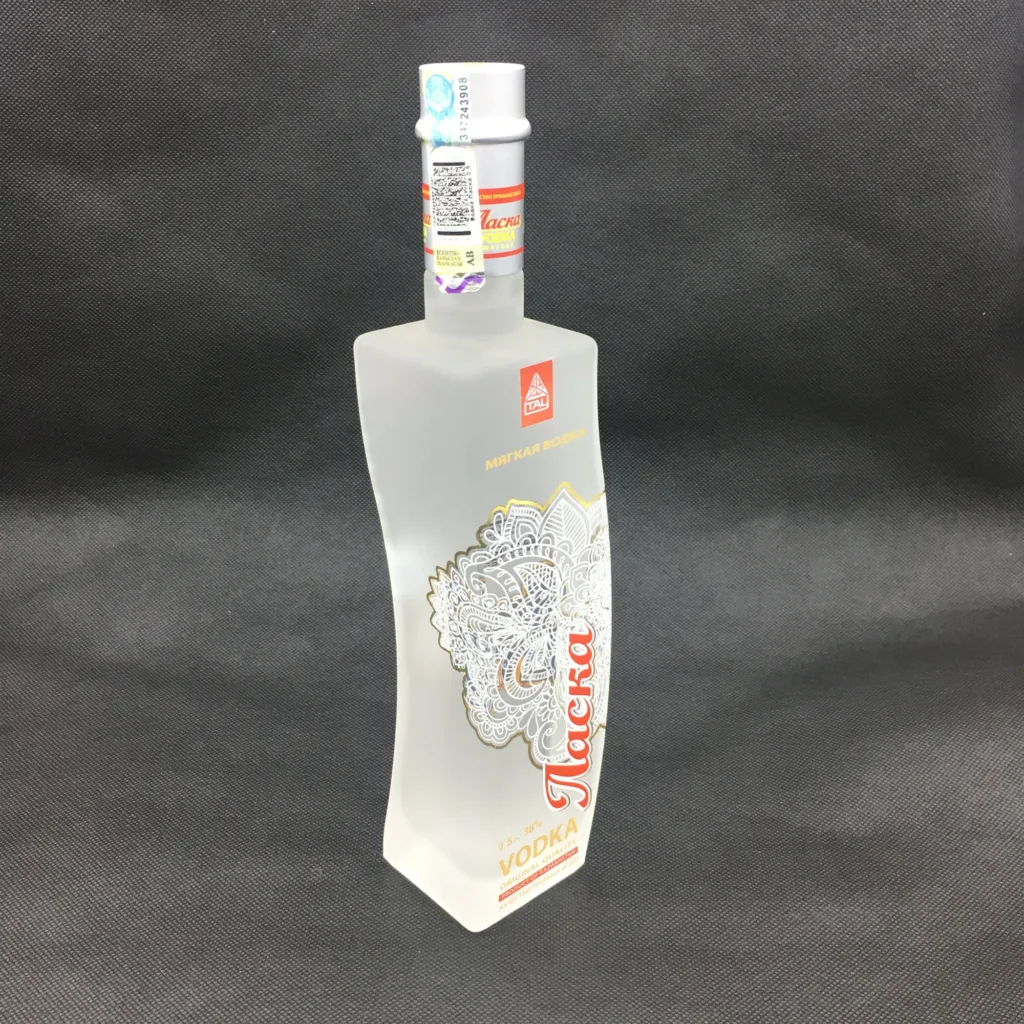 A custom twisted glass vodka bottle with an asymmetric curved silhouette and a premium frosted finish, featuring an intricate white and gold mandala pattern decal with bold red branding.