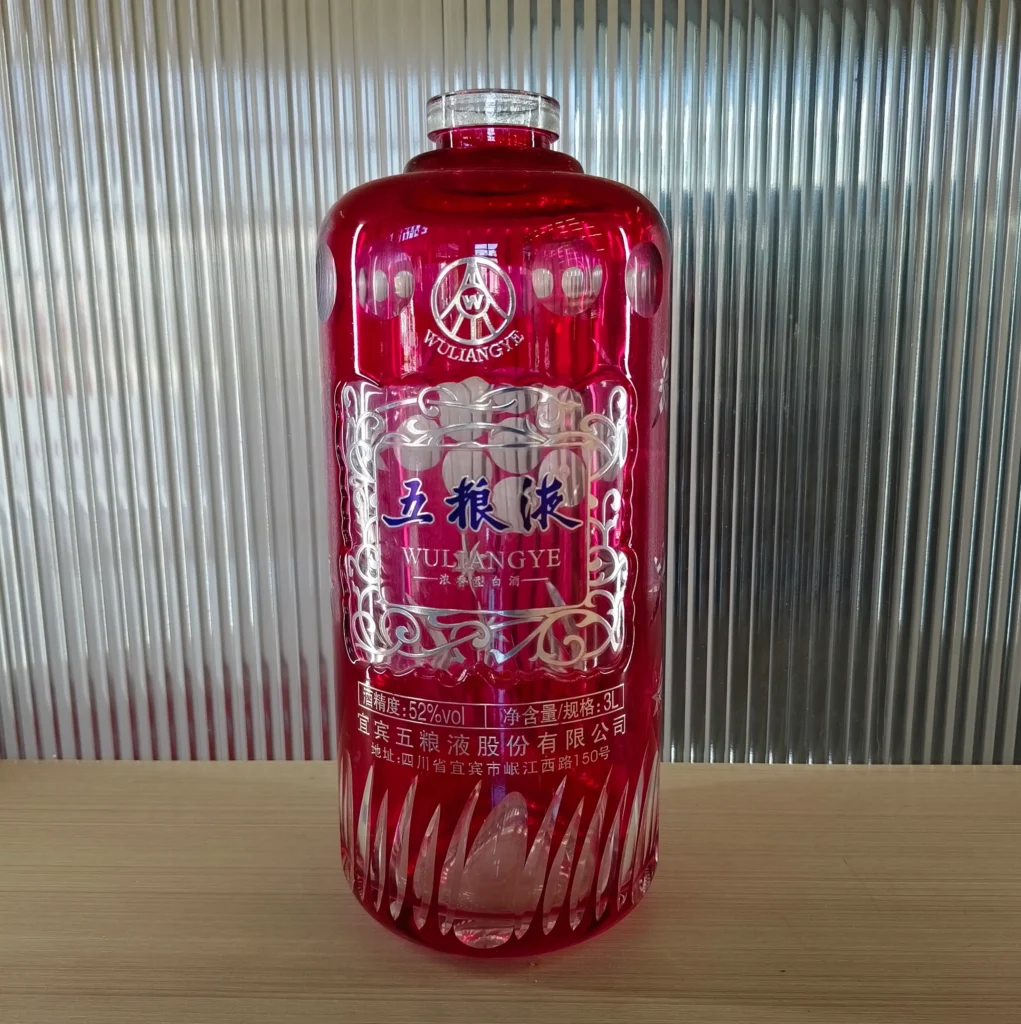 A custom translucent ruby red spirits bottle featuring luxury embossed decal effects with raised tactile metallic silver framing, embossed brand logos, and intricate crystalline base cuts.