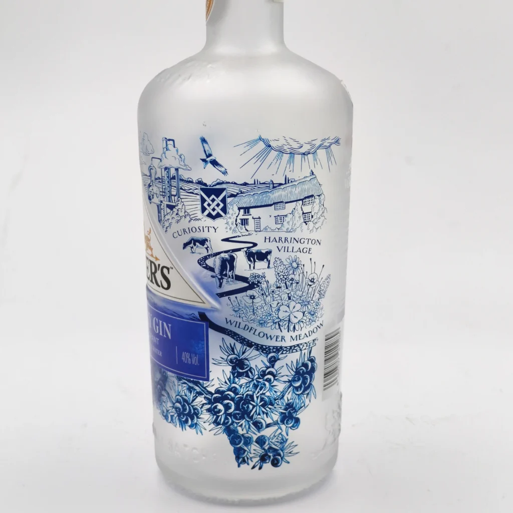 A custom frosted glass gin bottle featuring a high-precision blue line-art illustration with intricate historical village scenes, fine text typography, and detailed botanical patterns.