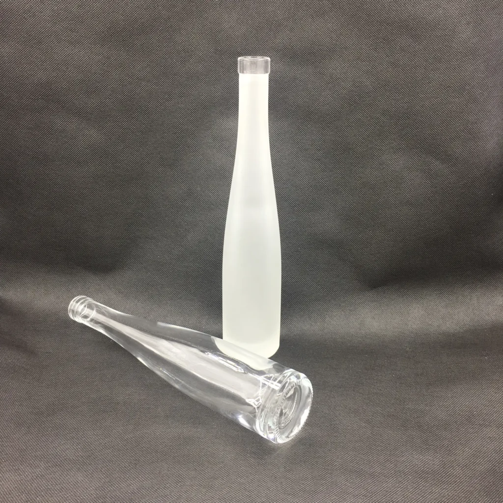 A commercial product comparison showcasing a standing glass bottle with a full-body frosted acid etching finish next to a lying transparent clear glass bottle of the same slender design.
