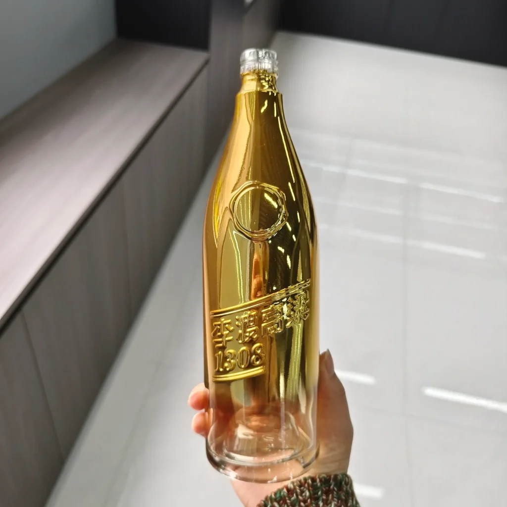 A custom spirits glass bottle showcasing a luxury gradient metallic gold electroplating finish that smoothly fades into a transparent clear base, highlighting sharp embossed brand lettering.