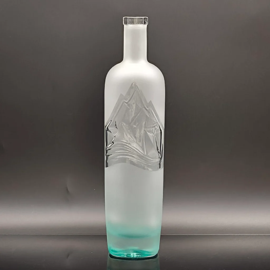 A premium frosted vodka glass bottle showcasing a seamless gradient ice blue color coating at the base, contrasting with a transparent 3D embossed mountain relief.