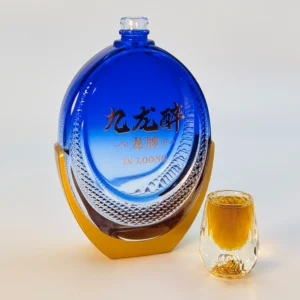 Our Approach A luxury custom oval-shaped glass spirits bottle showcasing a complex dual-color coating: a translucent gradient royal blue fade on the upper body and a high-precision metallic gold spray on the custom base, displayed next to a gold-infused crystal shot glass.