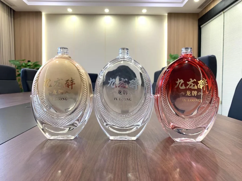 Three finalized production units of a premium spirits bottle series, featuring gold, clear, and red-gradient glass finishes with textured side detailing, arranged on a conference table to demonstrate high-quality manufacturing consistency.