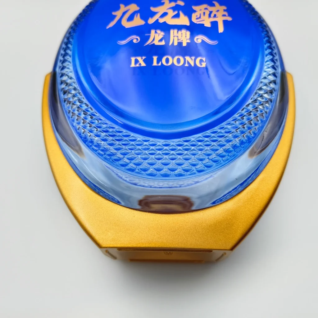 Close-up detail of a premium spirits bottle, showcasing a crisp, clean demarcation line between the blue glass and the gold-tone spray-coated base, alongside intricate embossed dragon-scale textured patterns.