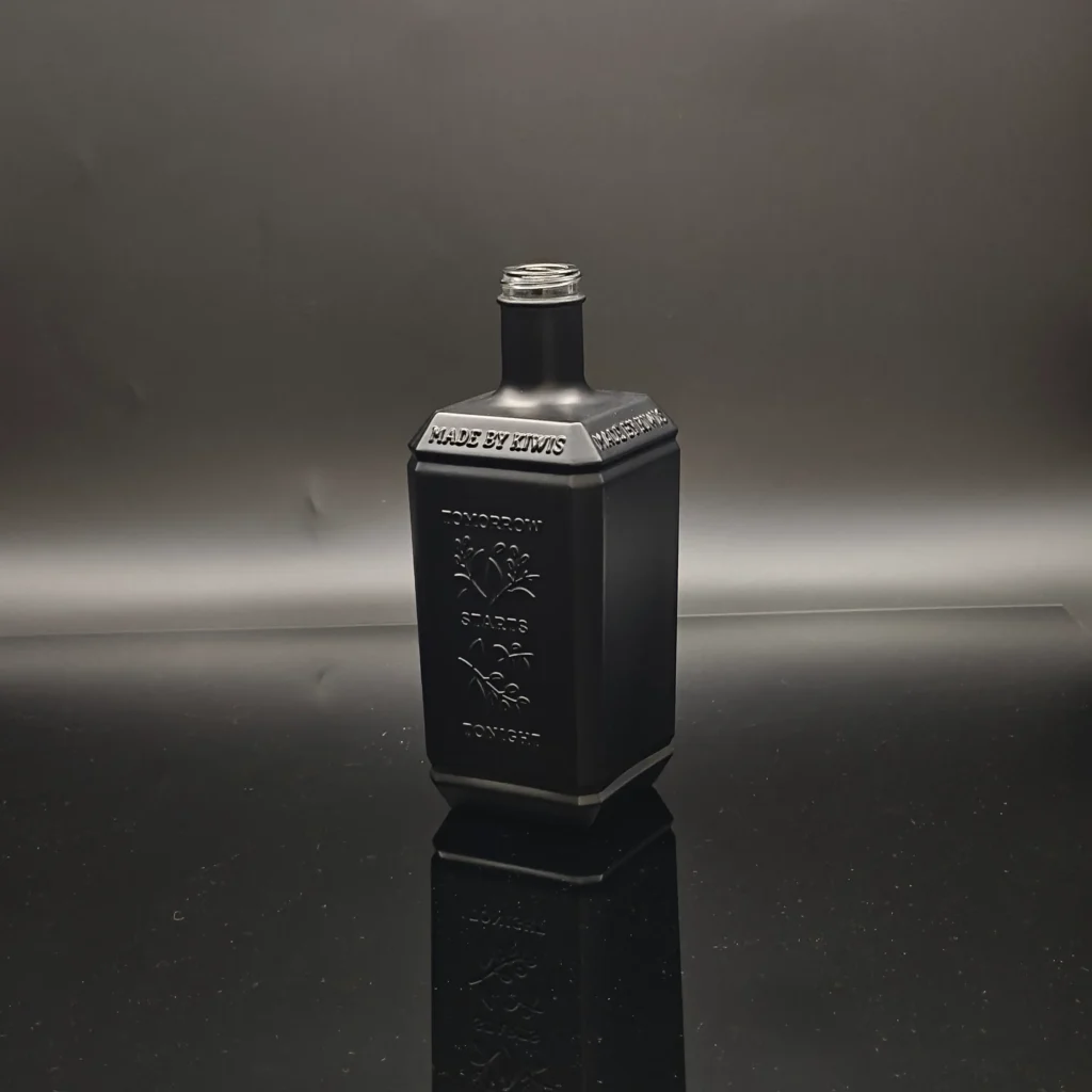 A custom square spirits glass bottle coated in a flawless opaque matte black solid color finish, sharp embossing details of plant motifs and text logos.