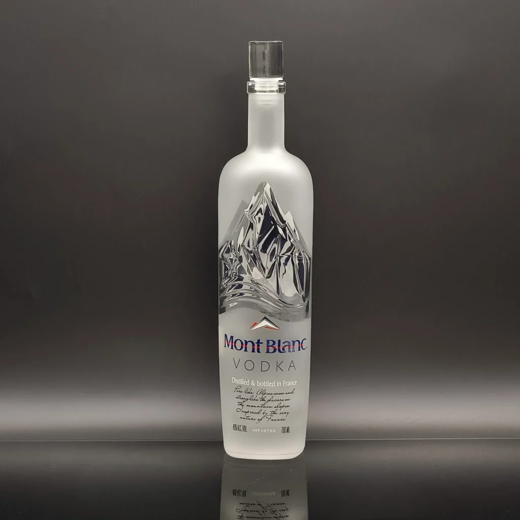 A custom 700ml vodka glass bottle showcasing partial frosting and window masking tech, where the intricate 3D embossed mountain relief remains perfectly crystal clear amidst a smooth acid-etched matte body.