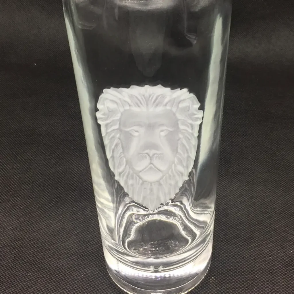 A custom clear spirits glass bottle featuring a precise partial sandblasting design, showcasing a highly detailed frosted lion head motif with sharp boundary lines on a super flint glass background.