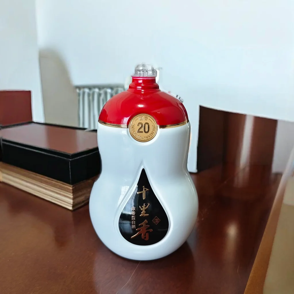 A custom gourd-shaped spirits bottle demonstrating precise multi-color branding with seamless red, white, and black color blocks accented by detailed metallic gold foil emblems.