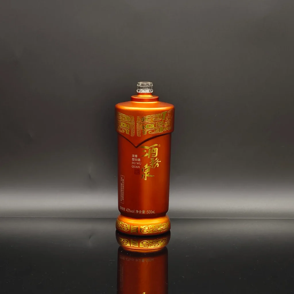 A luxury custom-shaped glass bottle featuring a matte metallic copper-orange coating and highly intricate, high-definition metallic gold water slide decaling patterns on the neck and base for 'Jiu Wu Quan' spirits brand.