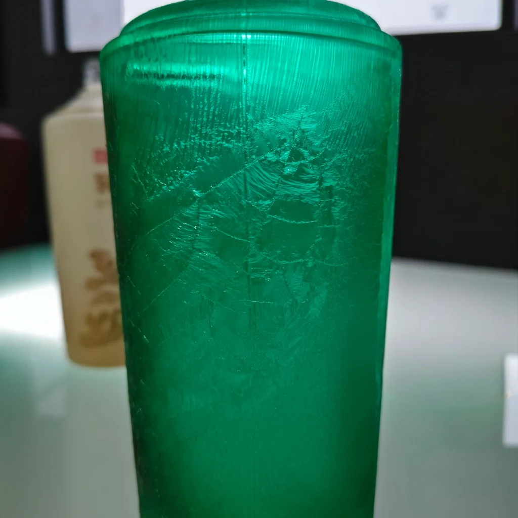 A close-up of a custom glass bottle featuring a translucent emerald green color coating with a premium tactile crackled ice and marbled texture effect.